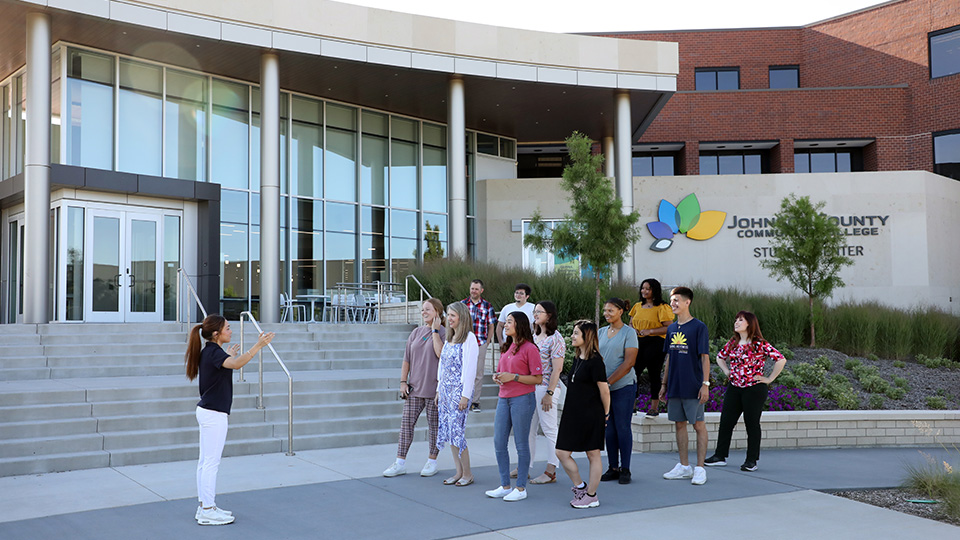 A JCCC admissions representative leading a group tour in front of the student center.