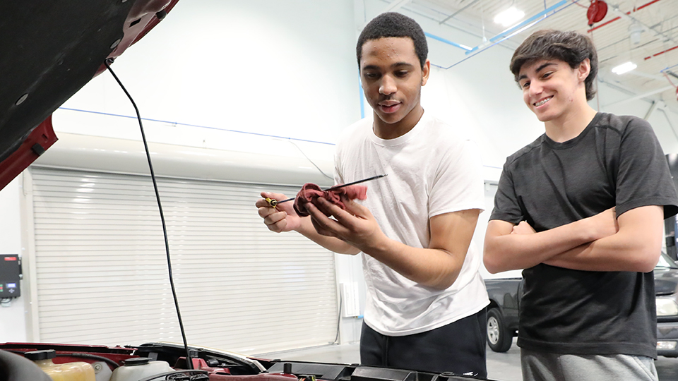 Two JCCC students check the dip stick of a car