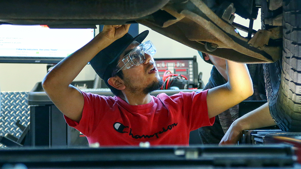 A JCCC student checks the undercarriage of a vehicle that is on a lift