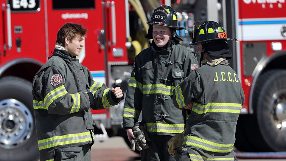 Three firefighters talk beside a fire engine.