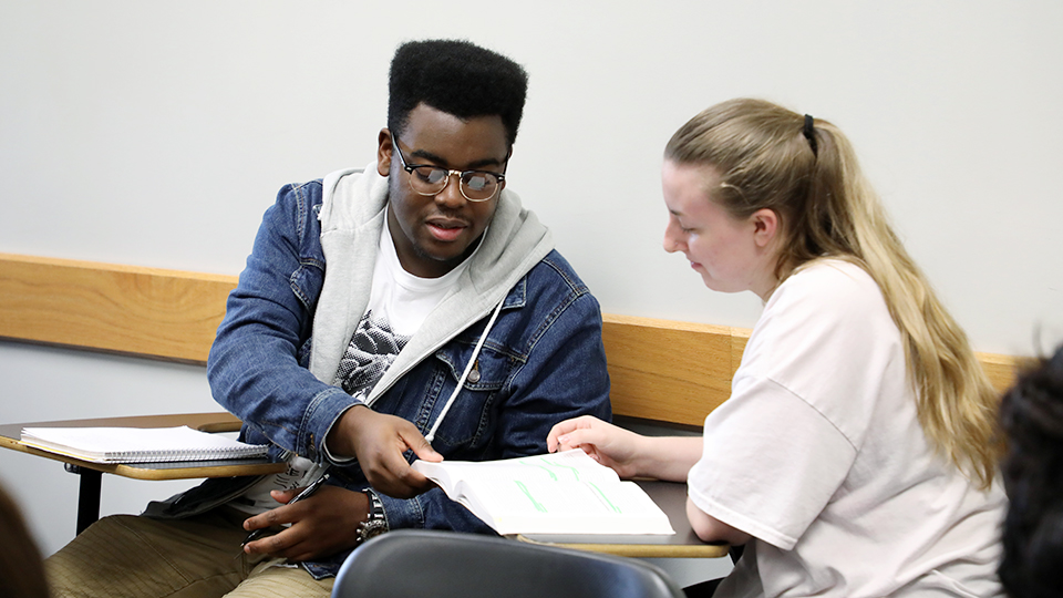 A student hands a paper to another student.