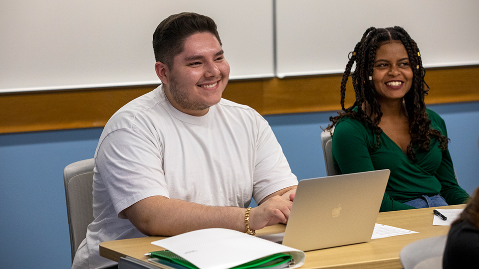 Two smiling students sitting at a table.