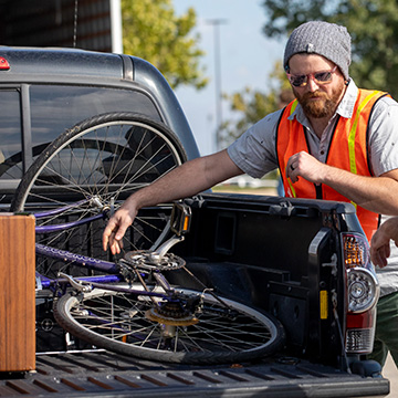 a man in a safety vest unloads a bike from the back of a pickup truck