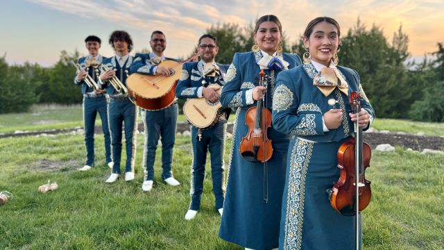 members of Mariachi Estrella standing in a line. They are holding their instruments and smiling at the camera. All are wearing traditional clothing. 