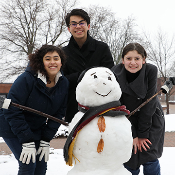 Three honors students posing by a snowman the built during the winter